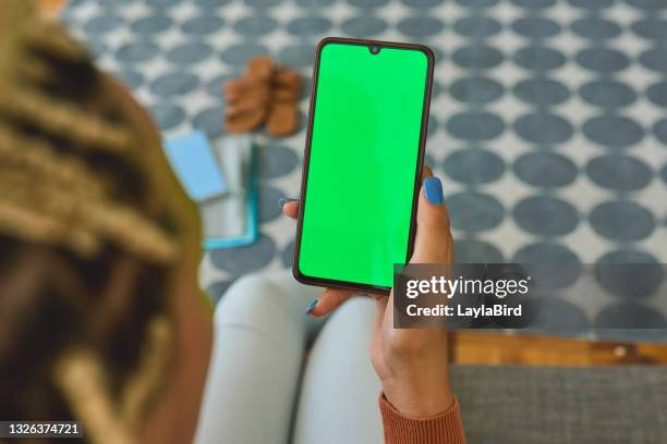 shot of an unrecognisable using a smartphone with a green screen on the sofa at home - green screen stock pictures, royalty-free photos & images