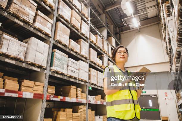 low angle view of asian woman using digital tablet working at a warehouse - low confidence stock pictures, royalty-free photos & images