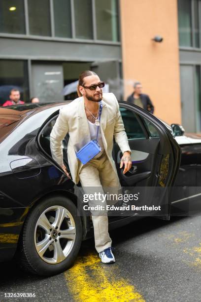 Rapper Julien Schwarzer aka SCH wears sunglasses, golden necklace, a beige blazer jacket, a blue crossbody Jacquemus bag, a white t-shirt, beige...