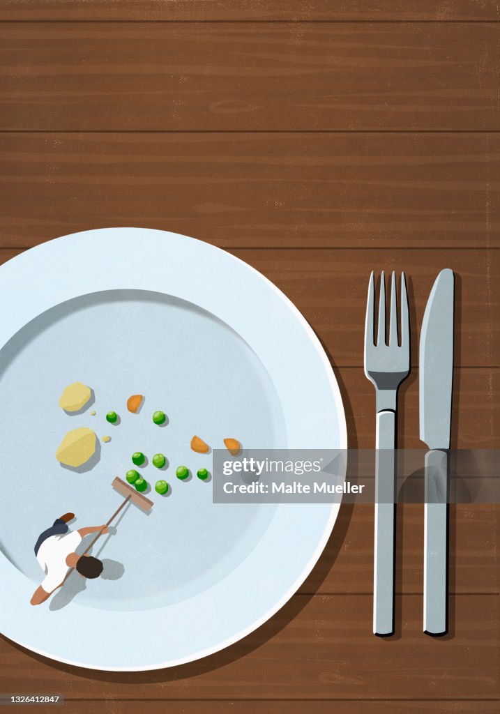 View from above man with broom sweeping food scraps on plate