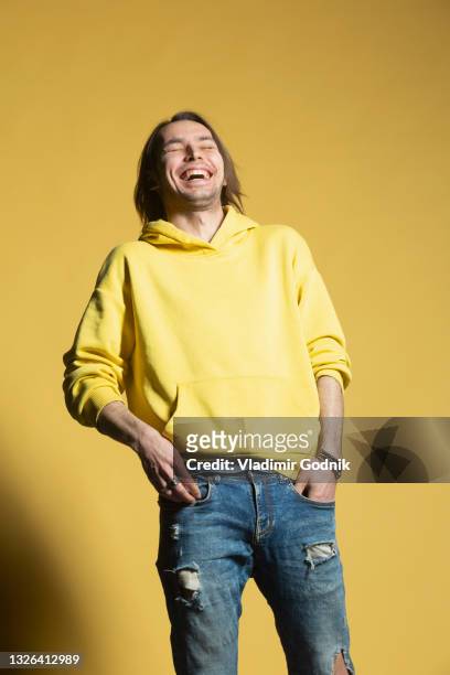 happy man in jeans and hoody laughing against yellow background - ripped jeans stockfoto's en -beelden