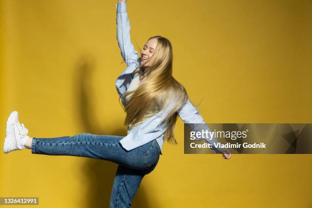 carefree young woman dancing on yellow background - blonde straight hair stock pictures, royalty-free photos & images