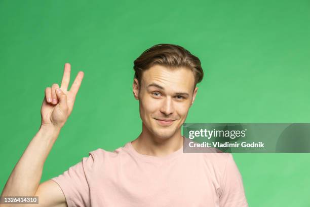 portrait confident young man gesturing peace sign on green background - victory sign man stockfoto's en -beelden