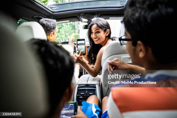 mother showing children vacation destination on smartphone - couple in car smiling stockfoto's en -beelden
