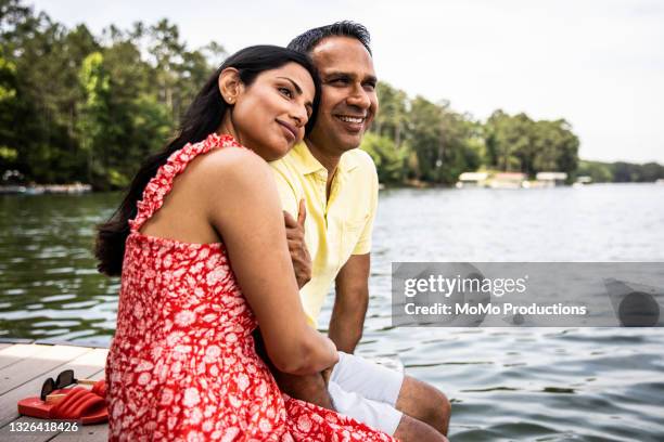 husband and wife sitting on dock at lake - asian and indian ethnicities fotografías e imágenes de stock