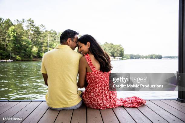 husband and wife sitting on dock at lake - women in see through dresses stock-fotos und bilder