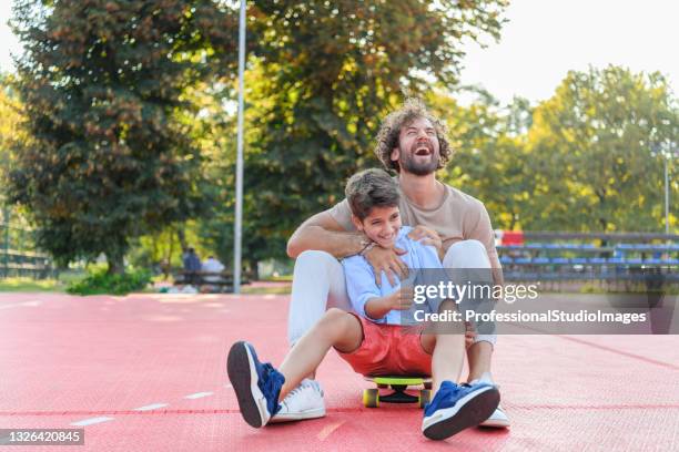 young father hat spaß mit seinem sohn, während sie gemeinsam auf einem skateboard reiten. - father longboard stock-fotos und bilder