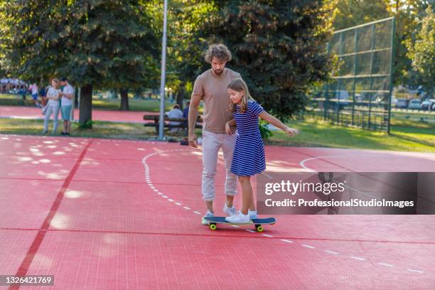 ein junger vater reitet mit seiner tochter in einem öffentlichen park auf einem skateboard. - father longboard stock-fotos und bilder