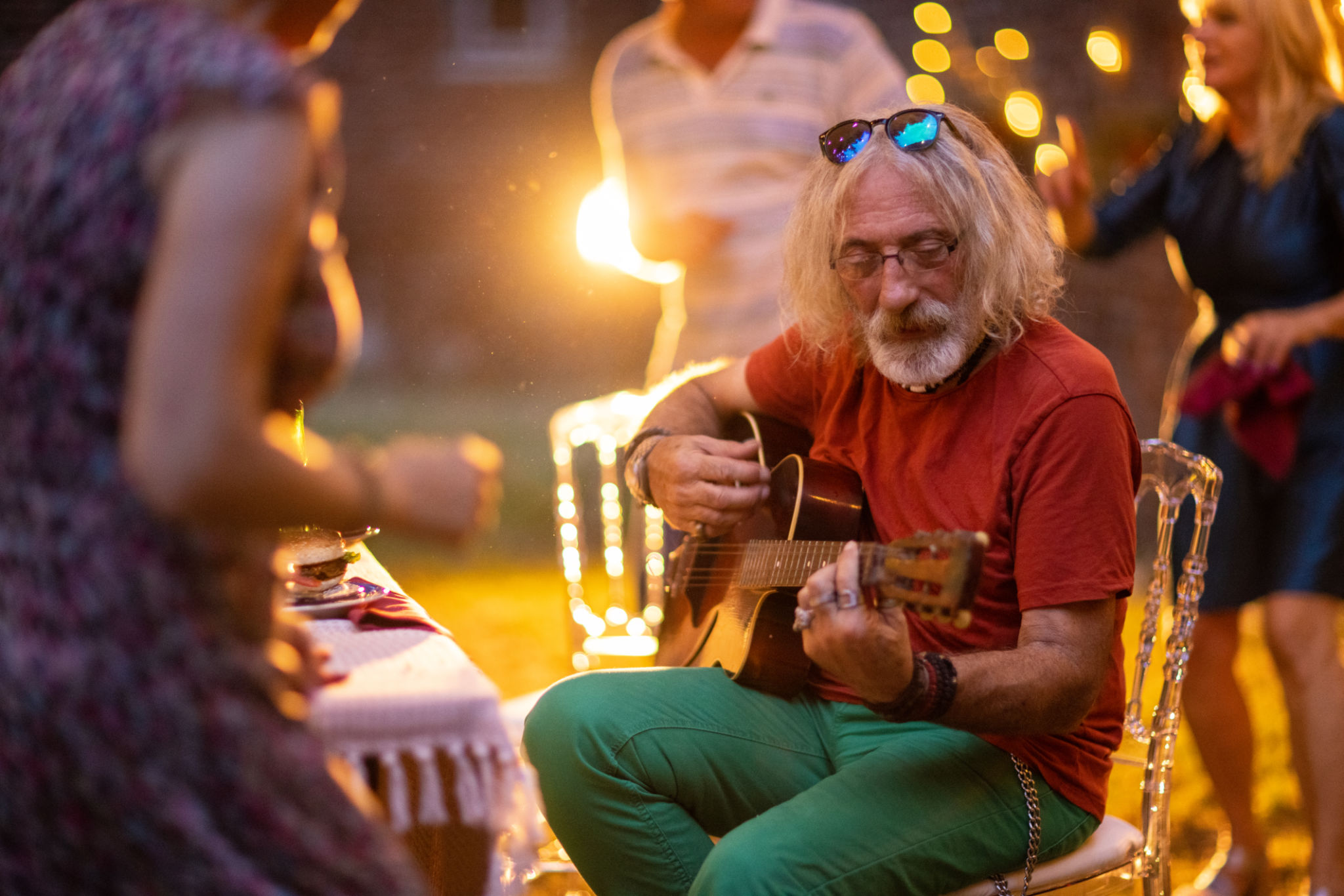 Senior man playing acoustic guitar for his friends on garden party Senior man playing acoustic guitar for his friends on garden party