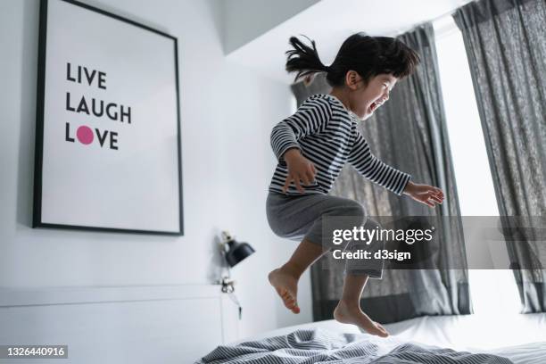 playful little asian girl jumping on the bed at home, having fun in bed. simple happiness - spring city break stock pictures, royalty-free photos & images