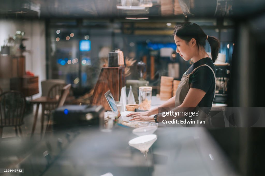 Asiatica cinese barista con laptop mentre si gode la cena al bancone del bar caffetteria
