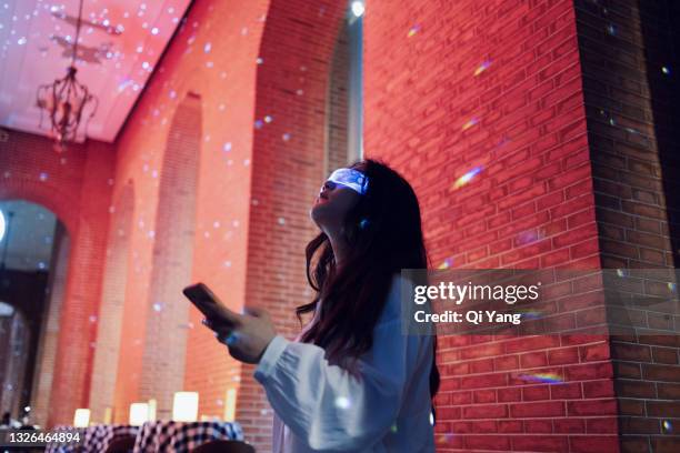 woman wearing augmented reality glasses standing in night street using smartphone - global solutions stock pictures, royalty-free photos & images