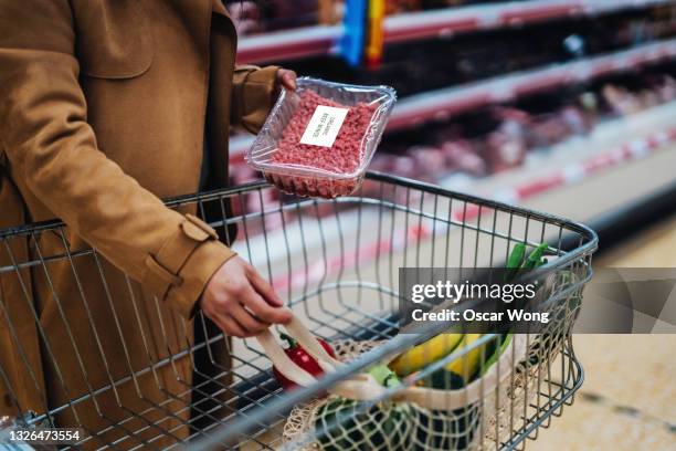 close-up of young woman placing a pack of fresh minced beef in shopping trolley - supermarket trolley female stock-fotos und bilder