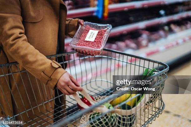 close-up of young woman placing a pack of fresh minced beef in shopping trolley - meat packaging stock pictures, royalty-free photos & images