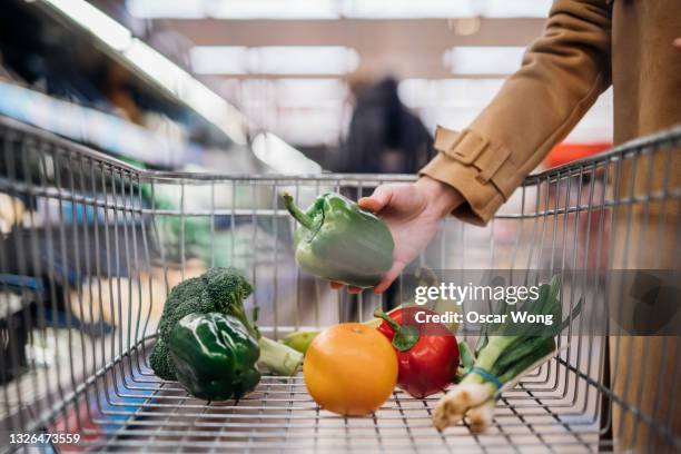 close-up of female hand placing fresh organic fruits and vegetables in shopping trolley - supermarket trolley female stock-fotos und bilder