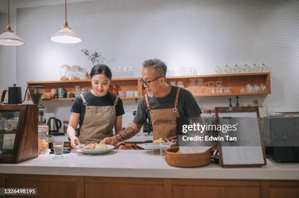 asian chinese senior male cafe owner passing plate of food to his daughters taking a break enjoying dinner at bar counter coffee shop  after work - asian family cafe stockfoto's en -beelden