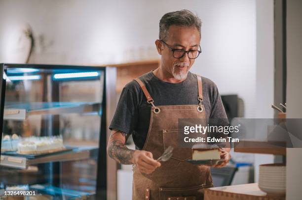 homme âgé chinois asiatique préparant une tranche de gâteau dessert à servir à son client du comptoir de la cuisine - pâtissier photos et images de collection