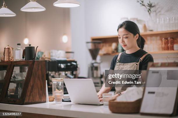 asian chinese female barista using laptop while enjoying dinner at coffee shop bar counter - part time job stockfoto's en -beelden