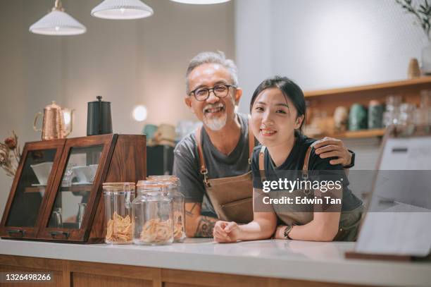 asiatische chinesische senior männliche café-besitzer und ihre töchter blickend auf die kamera lächelnd an der café-theke - neueröffnung stock-fotos und bilder