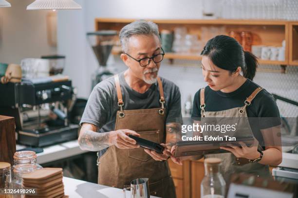 asian chinese senior man owner and daughter using digital tablet at bar counter table - asian family cafe stockfoto's en -beelden
