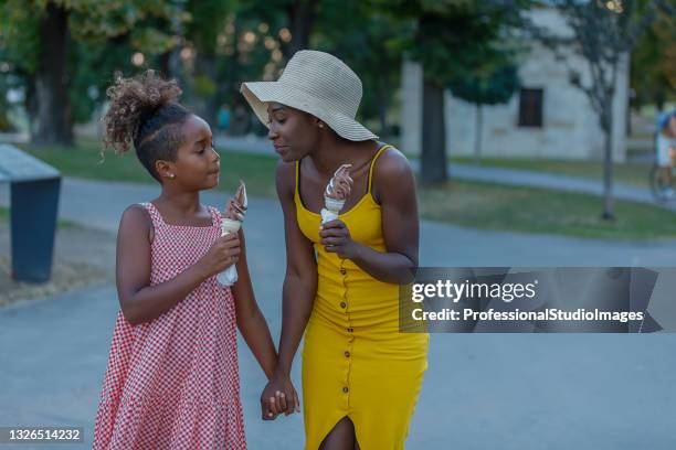 african-american mother and her cute little daughter are eating an ice cream in city park and holding hands. - model eating stock pictures, royalty-free photos & images
