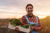 Happy female farmer holding a wood box containing fresh vegetables