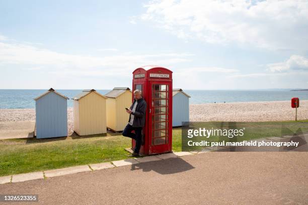man using smart phone outside red telephone box - red telephone box photos et images de collection