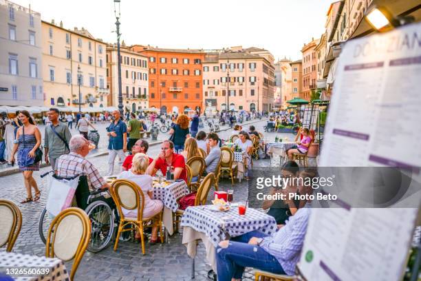 alcuni turisti si godono la vita seduti in un tipico caffè italiano a piazza navona, nel cuore barocco di roma - piazze italiane foto e immagini stock