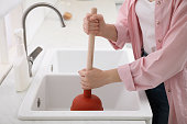 Woman using plunger to unclog sink drain in kitchen, closeup