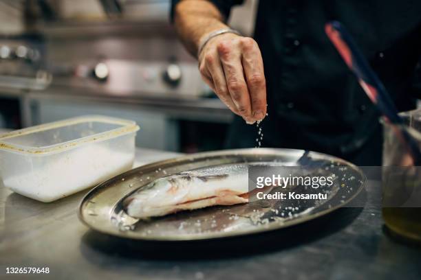 chef sazonando la lubina con una pizca de sal - sales occupation fotografías e imágenes de stock