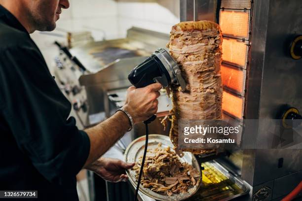 en la cocina del restaurante griego, el chef utiliza la herramienta eléctrica para cortar los giroscopios de pollo de la parrilla de giroscopios - pinchito fotografías e imágenes de stock