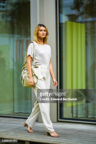 Chloe Lecareux wears a golden necklace, a white ribbed t-shirt, white suit pants, a large bag, beige sandals, during the Twilly By Hermes : Launch...