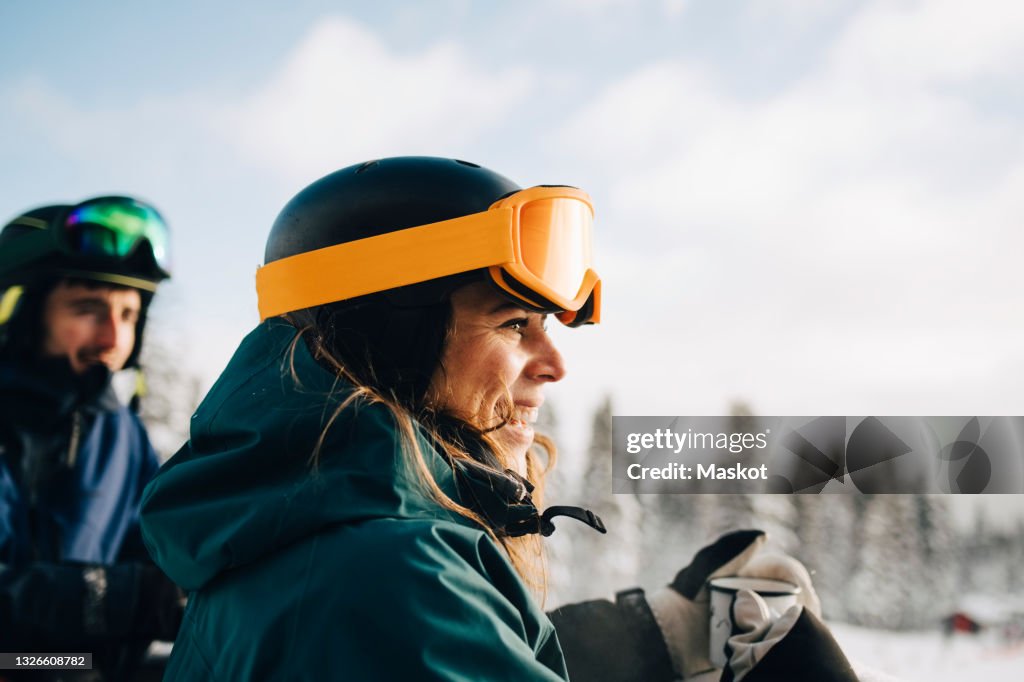 Smiling woman wearing ski goggles while holding coffee cup during winter