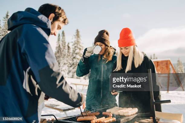 man preparing sausages while female friends standing at ski resort - jamtland stock pictures, royalty-free photos & images