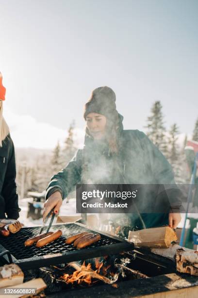 female friends preparing sausages on barbecue grill during winter - grillzange stock-fotos und bilder