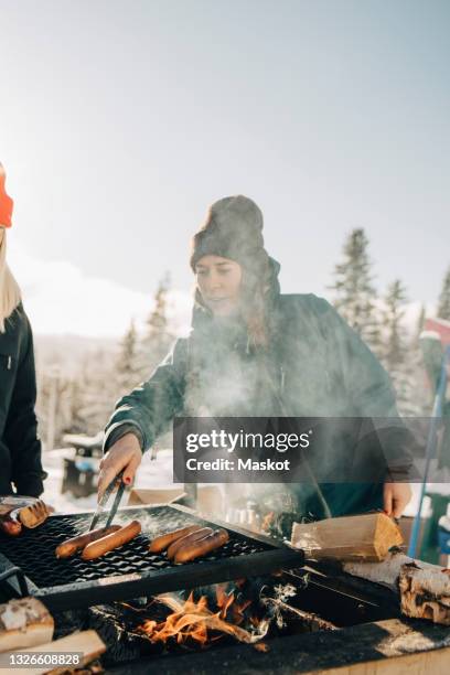 female friends preparing sausages on barbecue grill during winter - bbq winter ストックフォトと画像