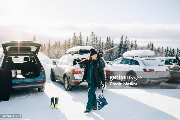 smiling woman looking away while walking on snow at parking lot - ski resort fotografías e imágenes de stock