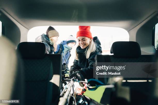 smiling woman loading skis in car trunk with friends - 3 guy friends road trip stock pictures, royalty-free photos & images