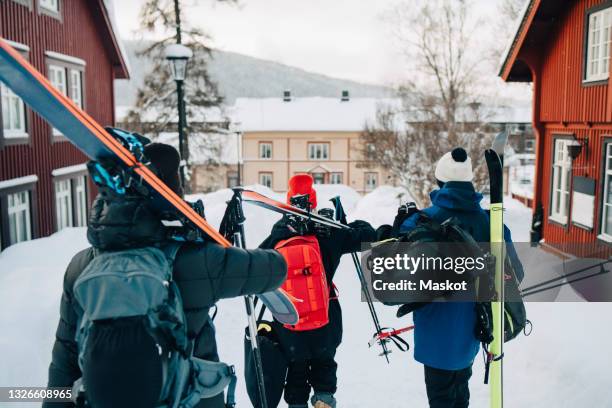 rear view of male and female friends walking with skis - ski resort stock pictures, royalty-free photos & images