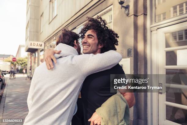 cheerful male friends hugging each other outside cafe - man embracing stock pictures, royalty-free photos & images