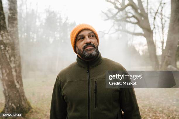 smiling male explorer looking away while standing in forest - fleece stockfoto's en -beelden