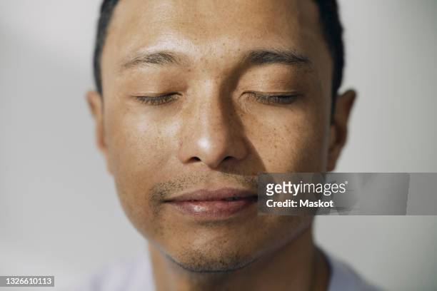 smiling man with eyes closed against white wall - man closed eyes stock-fotos und bilder