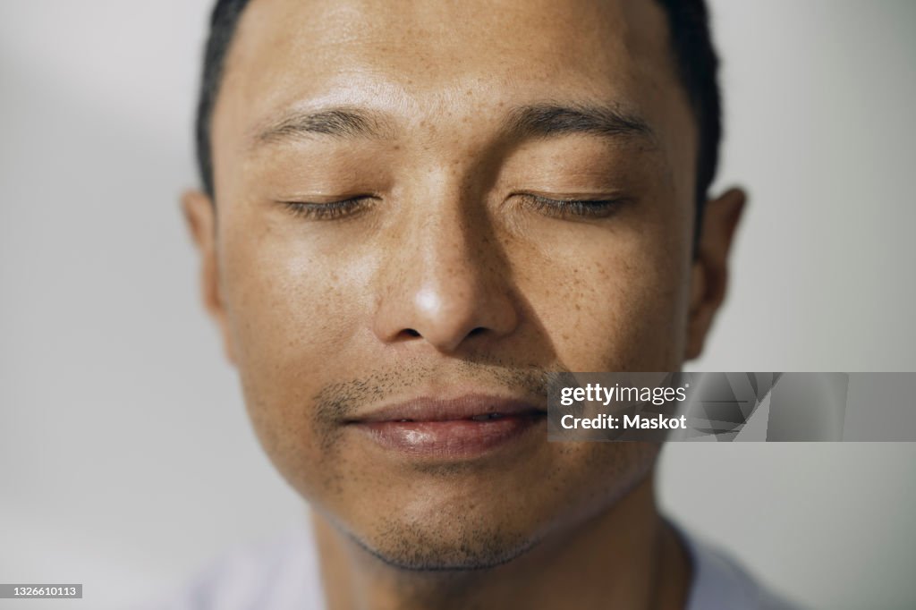 Smiling man with eyes closed against white wall