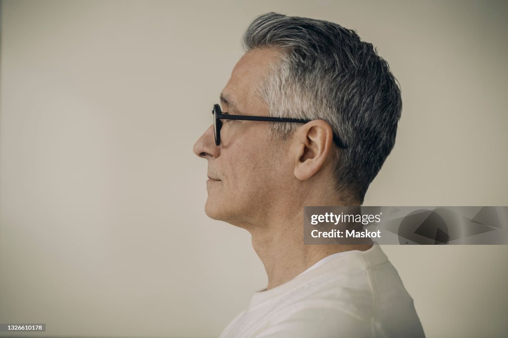 Profile view of mature man wearing eyeglasses against beige background
