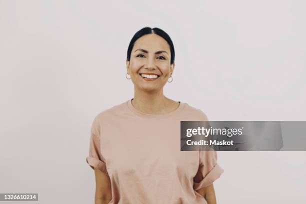 portrait of smiling woman wearing peach color t-shirt against white background - 35 year old woman stock pictures, royalty-free photos & images