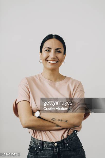 smiling woman standing with arms crossed against white background - arms crossed fotografías e imágenes de stock