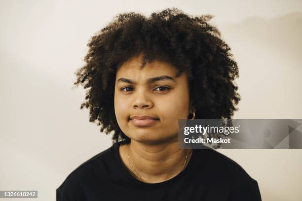 portrait of confused young woman with curly hair against beige background - suspicion - fotografias e filmes do acervo