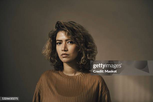 portrait of serious woman against beige wall - mid length hair stock pictures, royalty-free photos & images