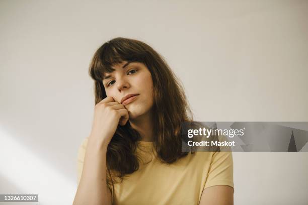 young woman with hand on chin in front of white wall - hoofd schuin stockfoto's en -beelden