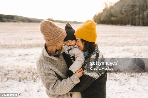 smiling lesbian mothers embracing daughter during sunset - baby hug stockfoto's en -beelden